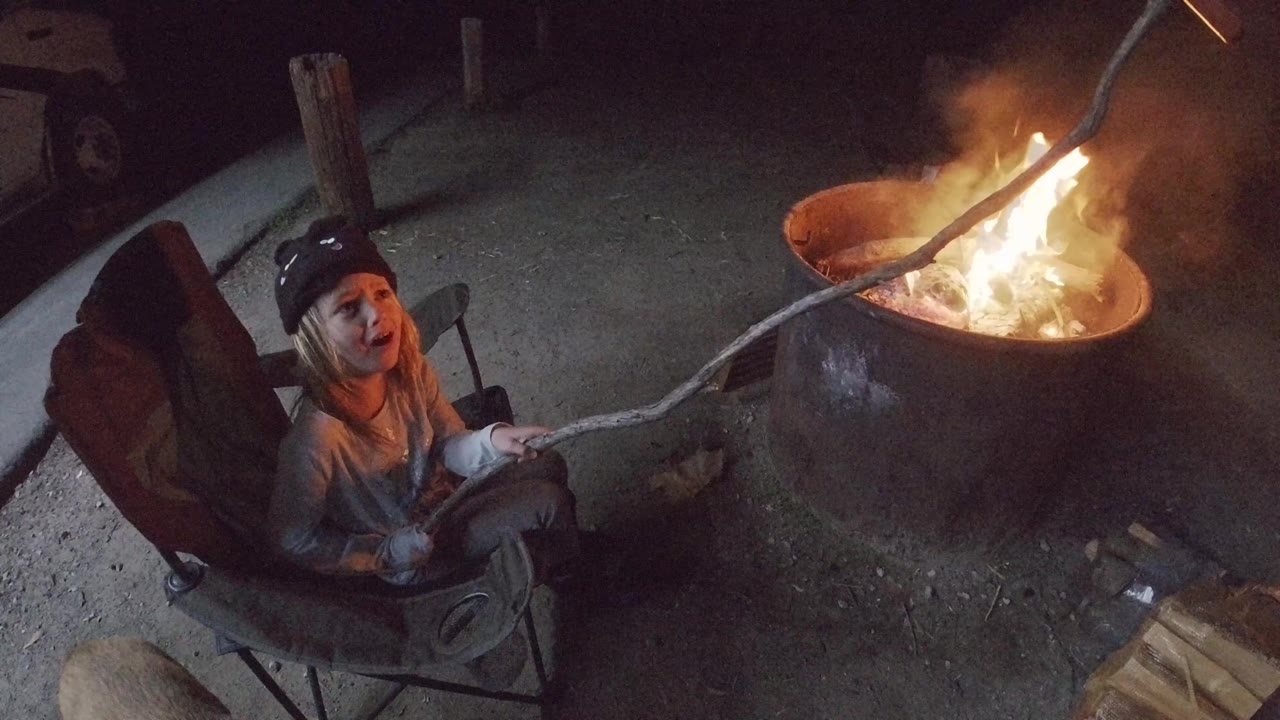 Child looks upward while holding a stick over a burning fire pit.