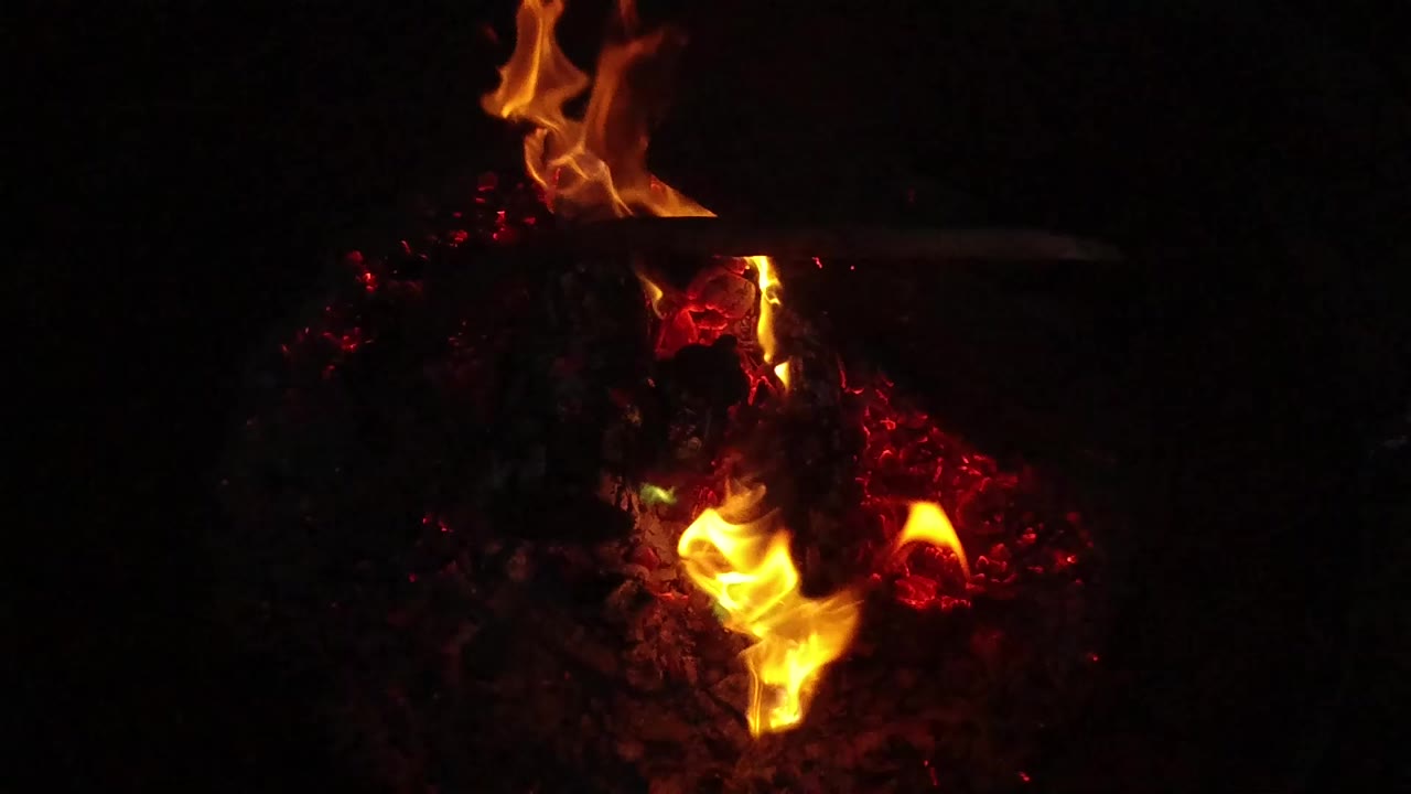 Close view of orange campfire flames rising from red embers in San Clemente, California, with a dark surrounding background and no visible people.