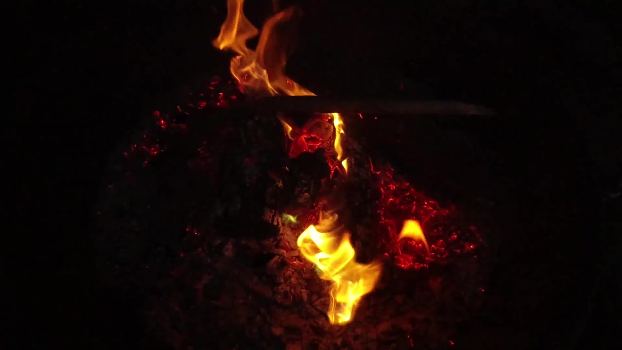 Bright flame curling above hot embers and charred wood.