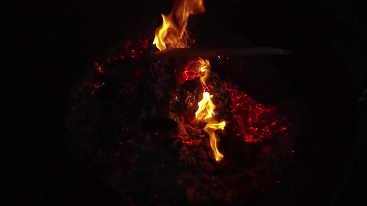 In San Clemente, California, a taller flame rises above the central logs while red coals glow to the right, with no visible people in this frame.