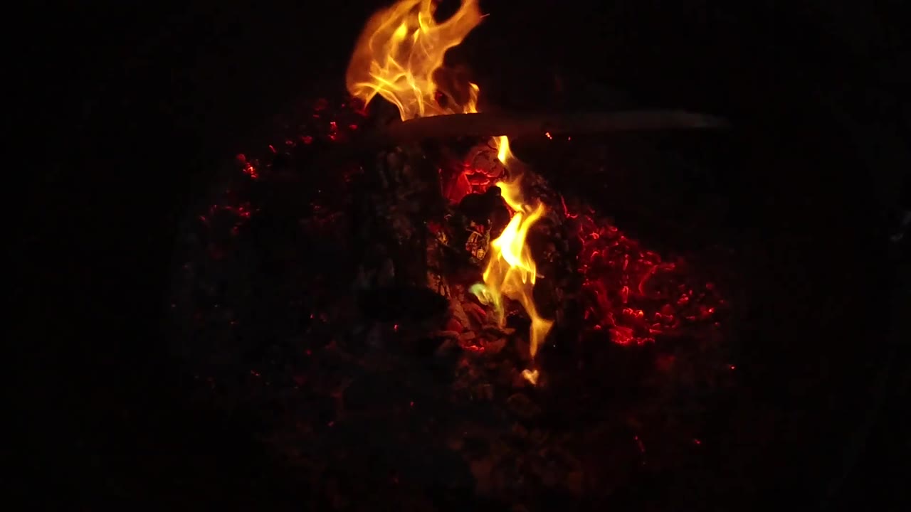 Large flame leaning over burning logs at night.