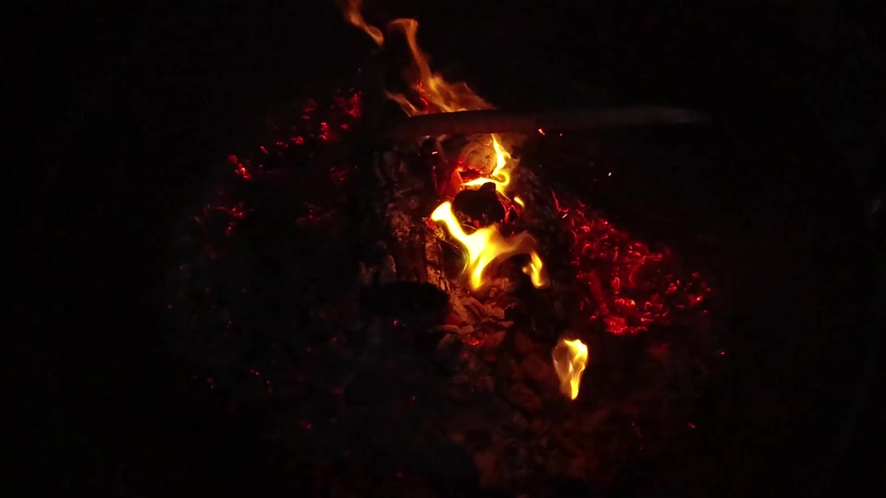 Orange flames burn over red embers in a dark San Clemente, California frame, with charred material visible and no visible people.