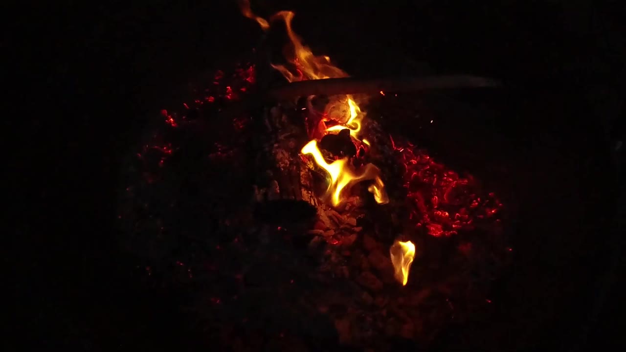 A brighter flame curls upward from the ember bed in San Clemente, California, with the rest of the frame falling into shadow and no visible people.