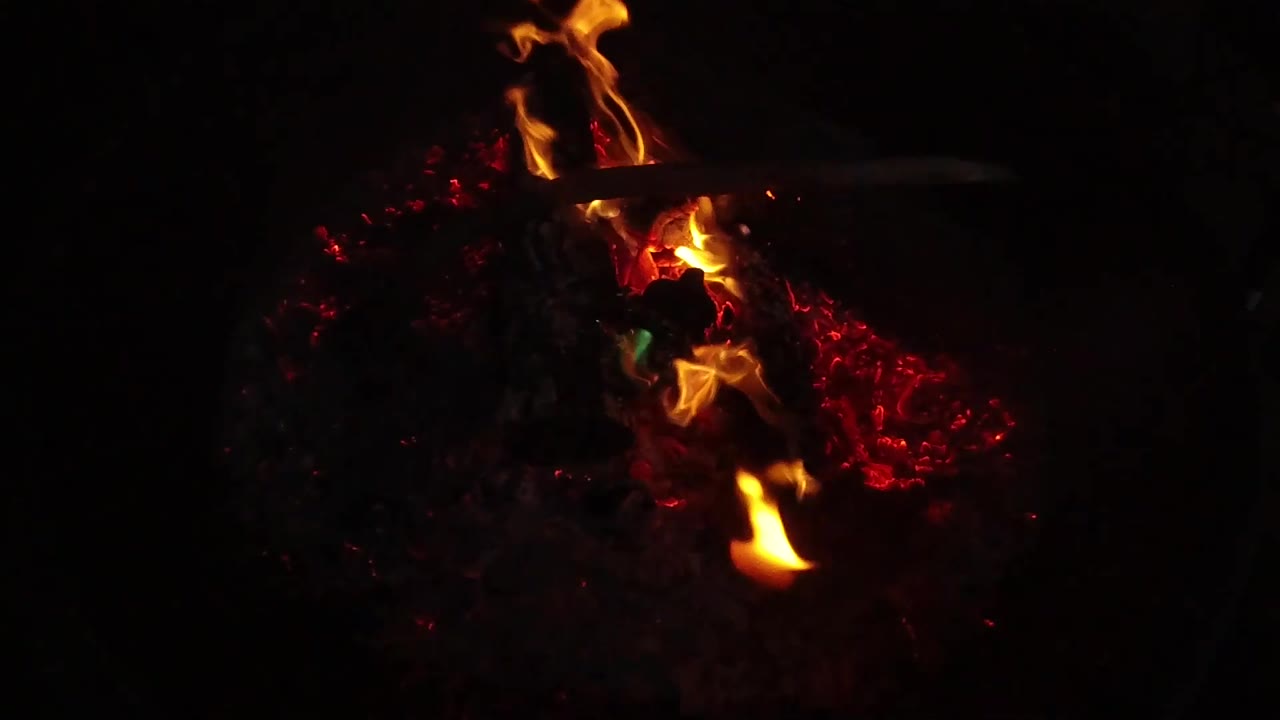 Tall orange flames rise from red coals in the dark San Clemente, California shot, with a small green fragment near the burning area and no visible people.