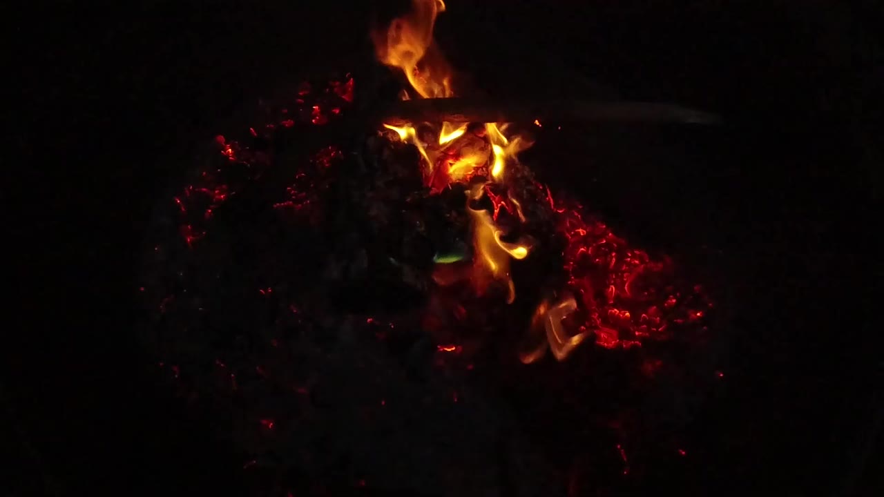 At 0:00, orange flames curl above a bed of glowing red coals in San Clemente, California, with the rest of the frame mostly black and no visible people.