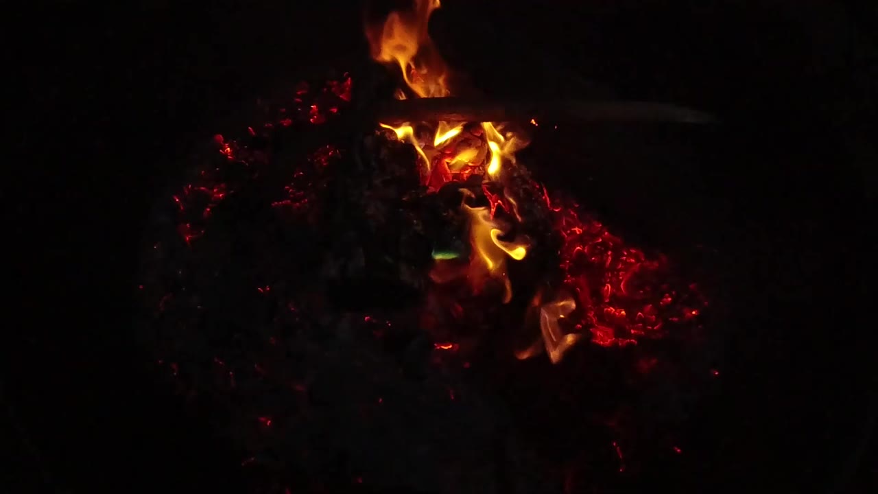 Campfire flames bending over red embers against a black background.