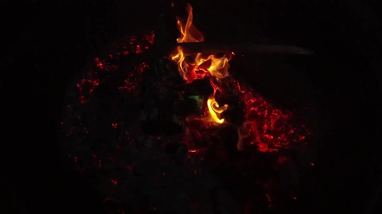 At 0:02, a taller orange flame lifts from the top of the glowing coals in San Clemente, California, while the surrounding background remains black and no people are visible.