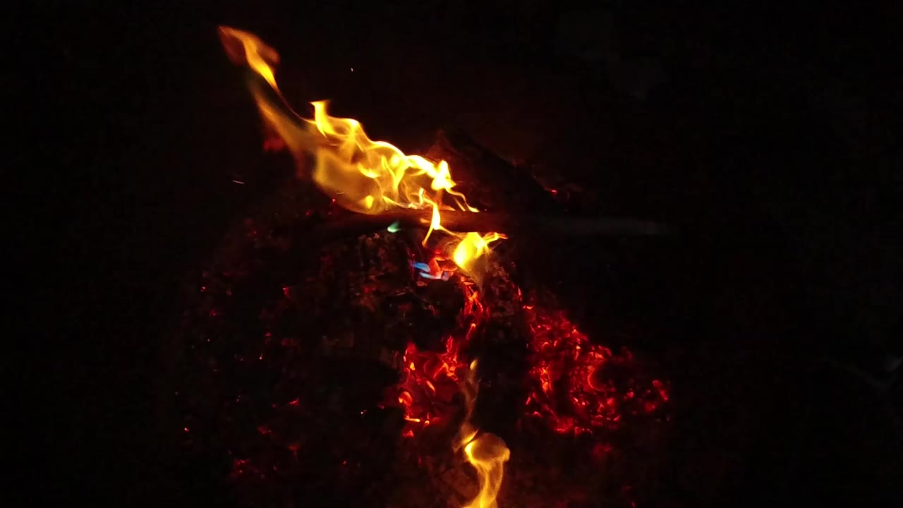 Orange flames lean upward over red embers in a dark grey fire pit in San Clemente, California, with no visible people.
