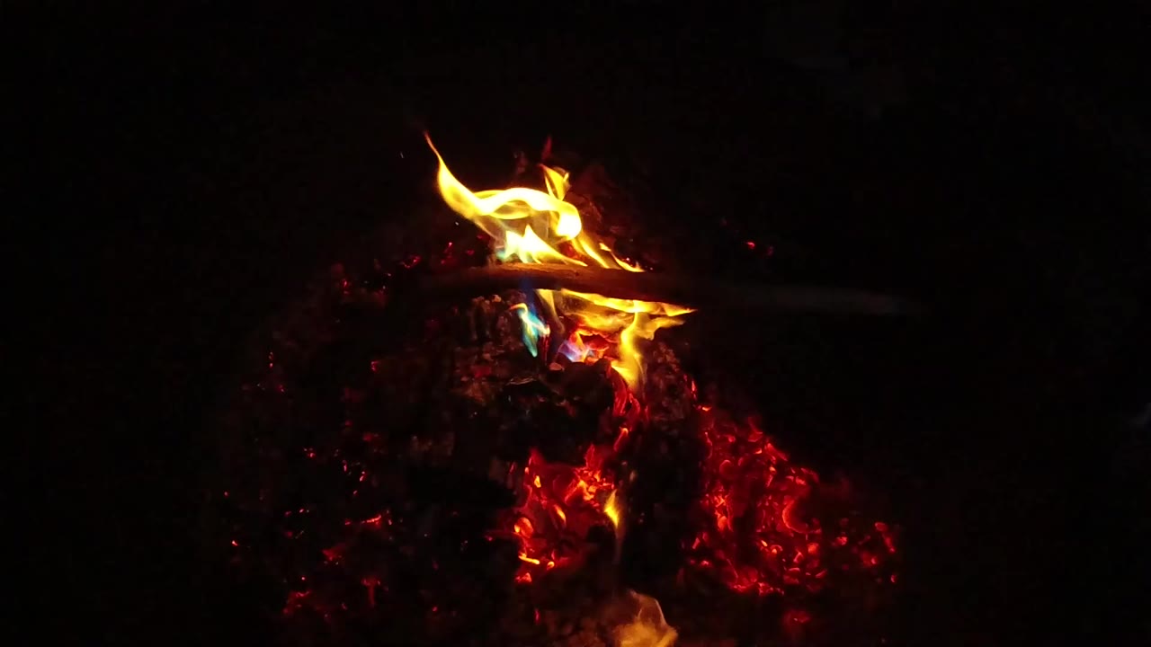 A small yellow flame burns above red embers in the San Clemente, California clip, with a black surrounding and no visible people.