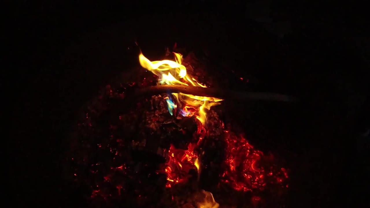 A yellow flame curls upward from a glowing red ember bed in the San Clemente, California footage, with no visible people.