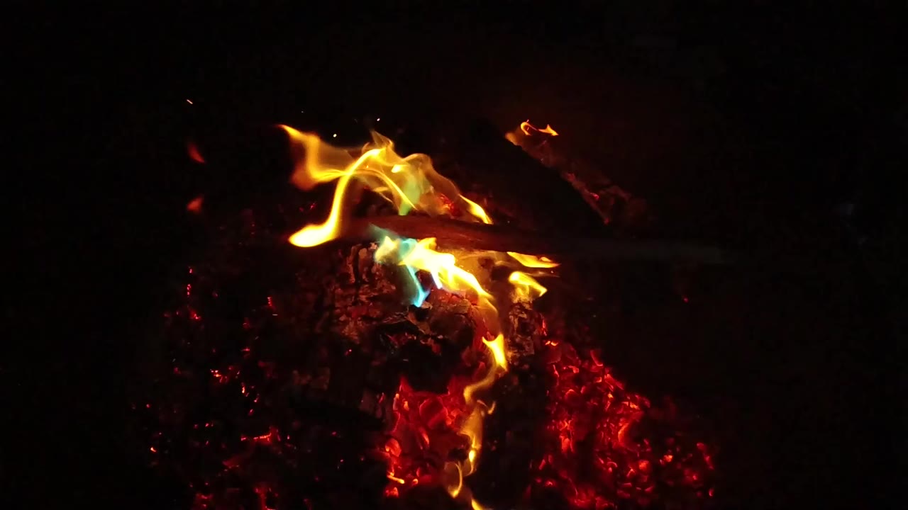 Close view of yellow-orange flames licking across charred wood and red embers in San Clemente, California, with no visible people in this frame.