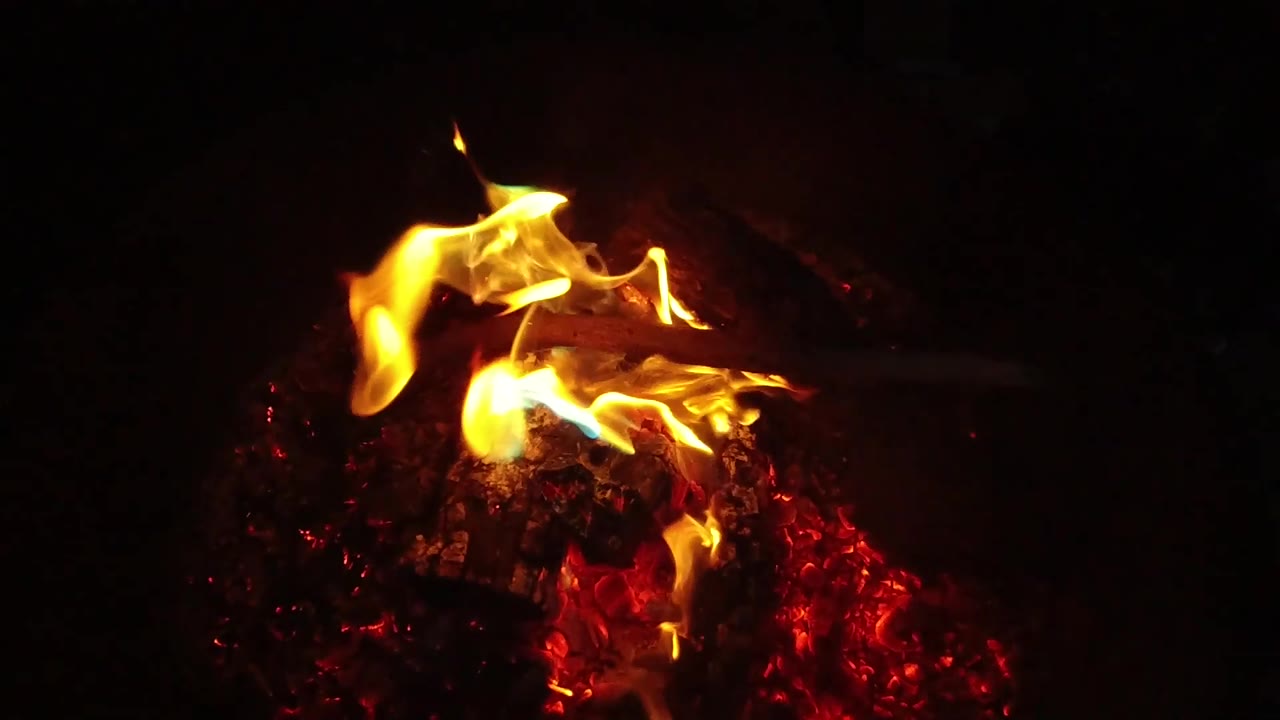 Brighter flames rise higher from the charred wood, with hot red coals concentrated at the lower right and no visible people in the frame.