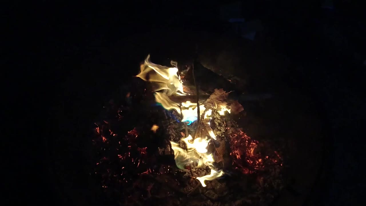 At 0:01, the flames curl higher over the ember bed in the San Clemente night scene, with a small blue flame visible near the lower center and no visible people.
