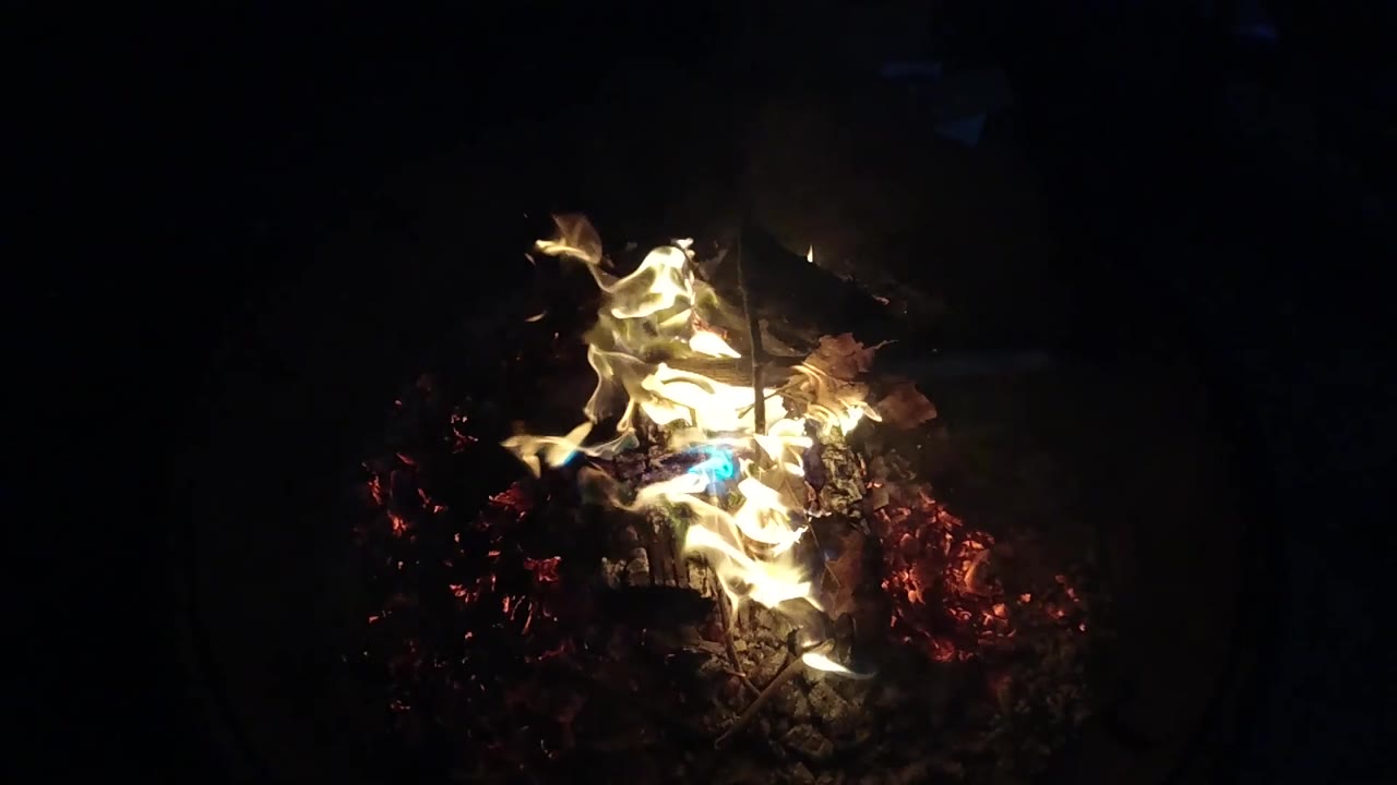 At 0:03, blue flame appears more clearly beneath the yellow fire in the San Clemente fire pit, with red embers to one side and no visible people.