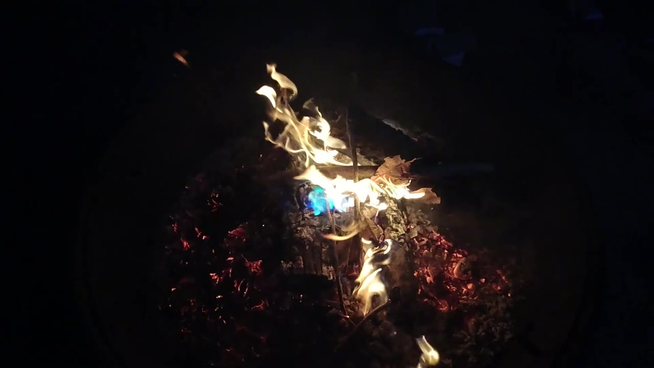 The fire sits slightly right of center in the dark frame, with glowing embers below the logs and no visible people.