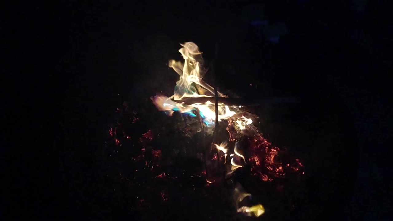 Burning wood pile in a dark fire pit at night