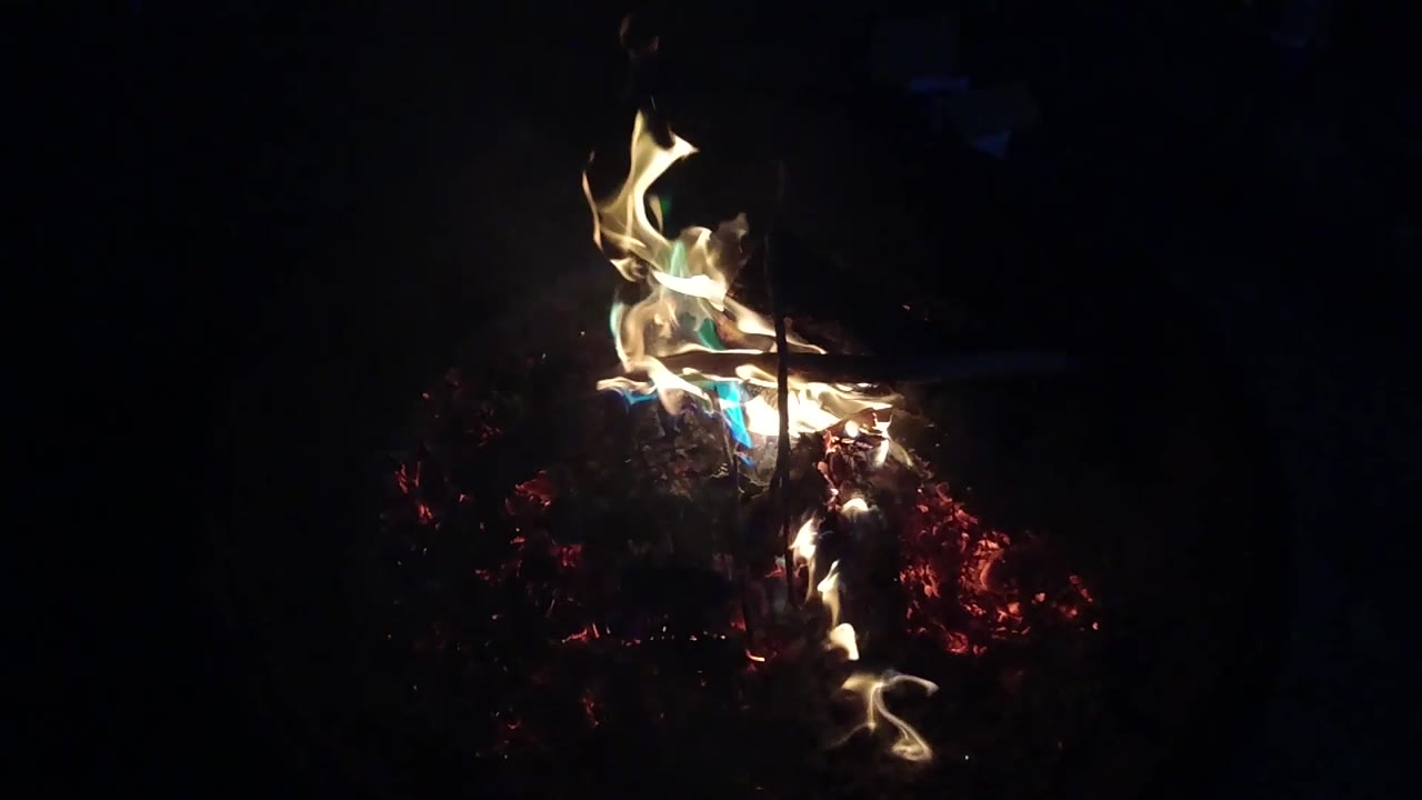 A bright flame curls over the right side of the burning wood pile in San Clemente, California, with black surroundings and no visible people.