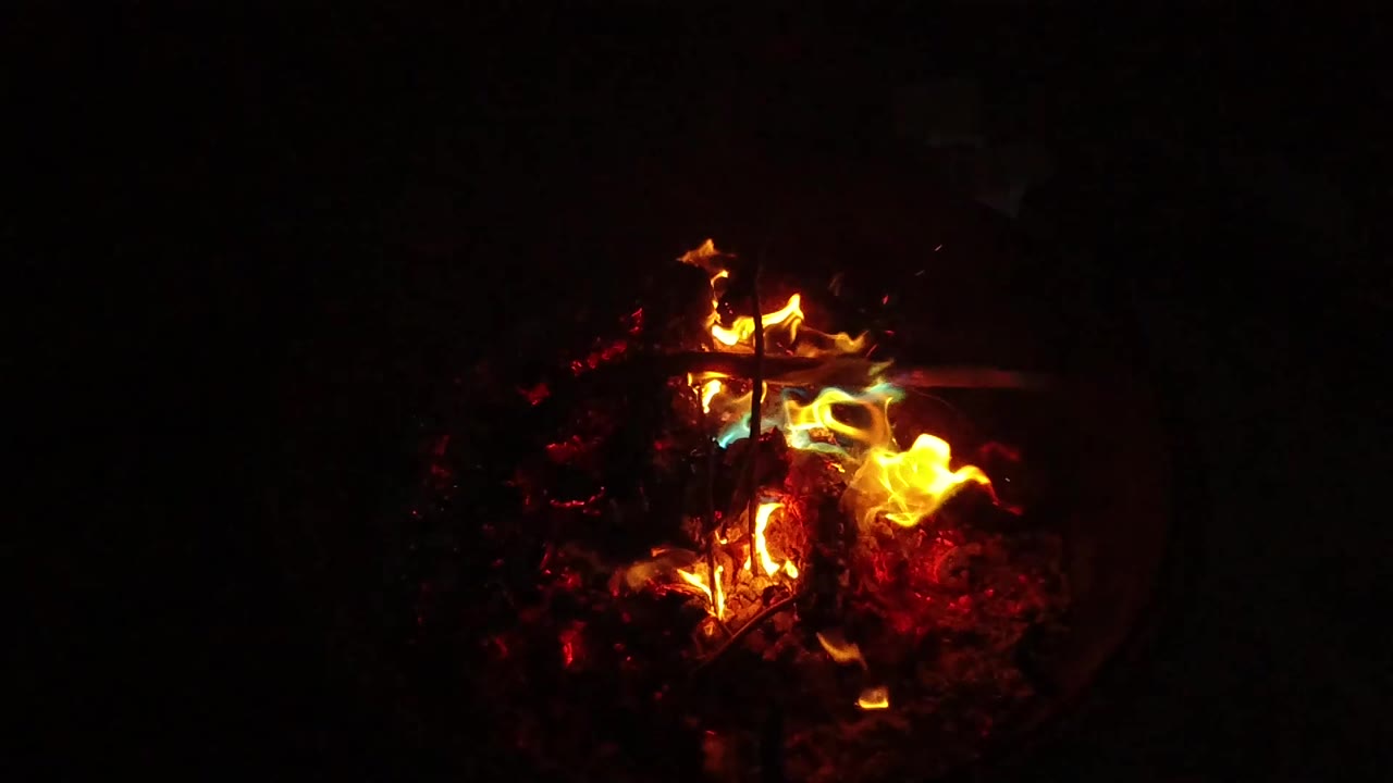 Bright flames curling over glowing wood in darkness.