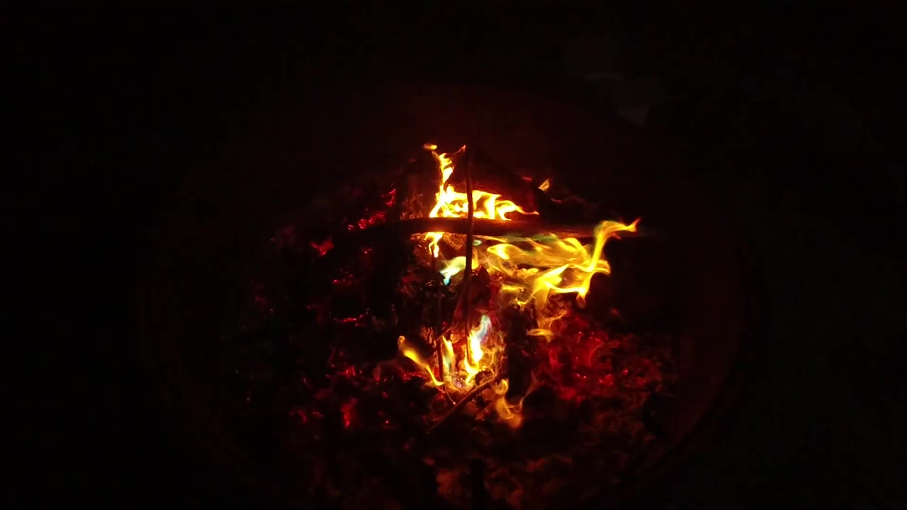 At 0:02, a strong yellow flame curls toward the right side of the San Clemente fire pit while red embers glow below and no visible people appear.