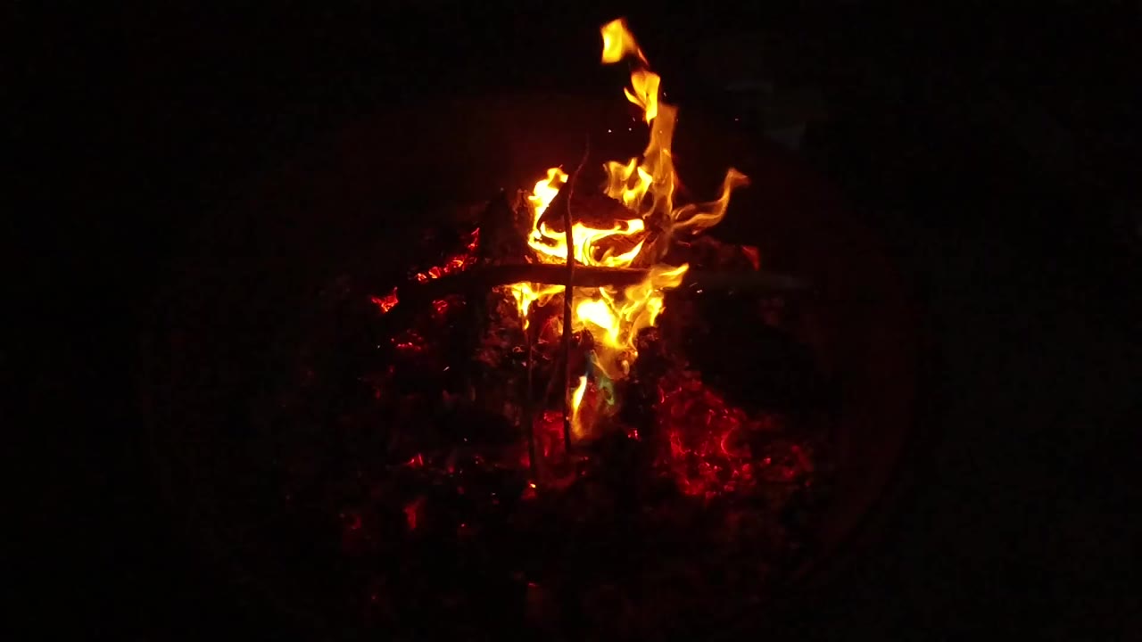 Bright flame over red embers in darkness