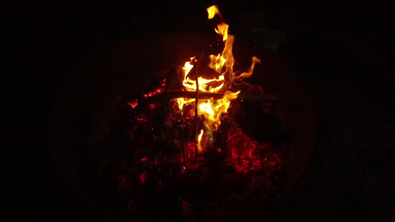 The flame curls upward from a compact bed of red embers in San Clemente, California, with the surrounding frame mostly black and no visible people.