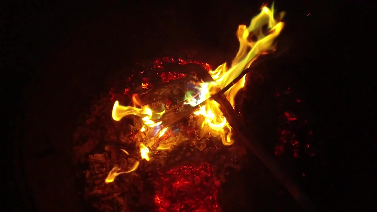 A brighter flame flare rises from the right side of the controlled bonfire in San Clemente, California, while red embers glow beneath and no visible people appear.