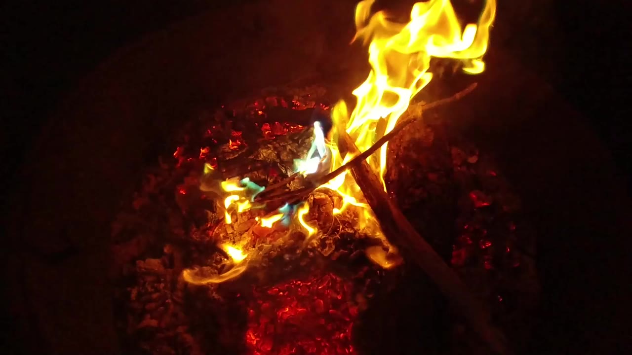 Bright campfire flames over red embers in darkness