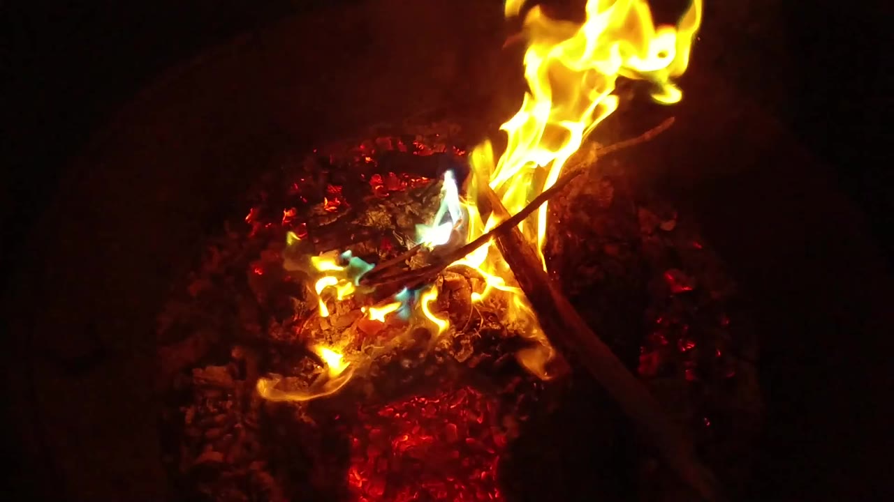 A taller flame leans across dark sticks over a bed of red embers in San Clemente, California, with no visible people.