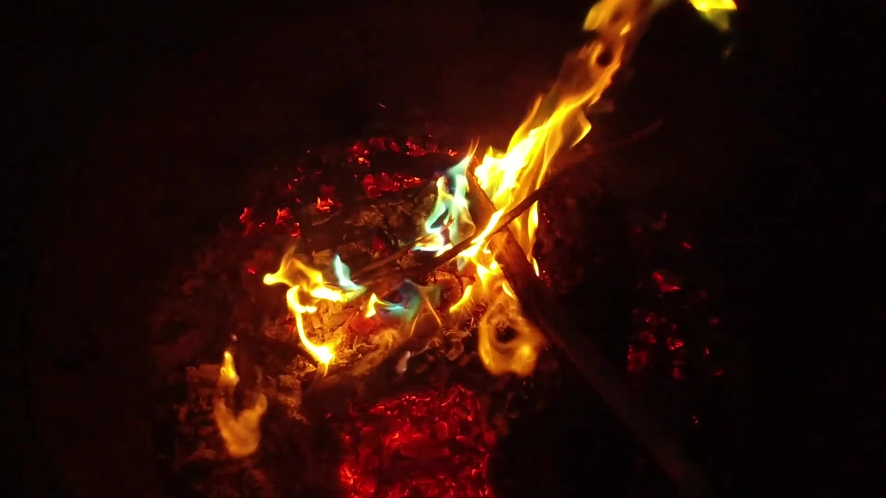 Blue-green flame highlights appear beside yellow fire on charred wood and embers in San Clemente, California, with no visible people.