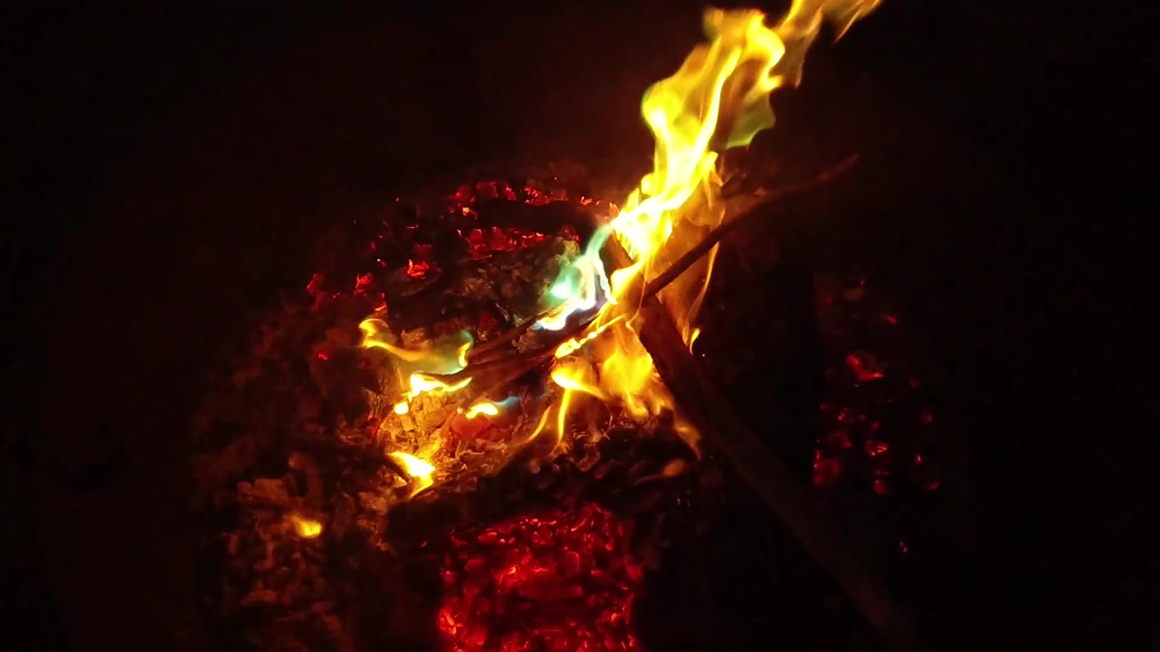 High yellow flames cross a dark branch over glowing red embers in San Clemente, California, with no visible people.