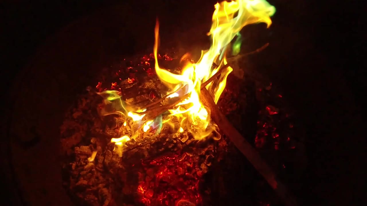 At 0:02, bright flame curls around the upper twigs while the coal bed glows red in the dark San Clemente fire close-up, with no visible people.