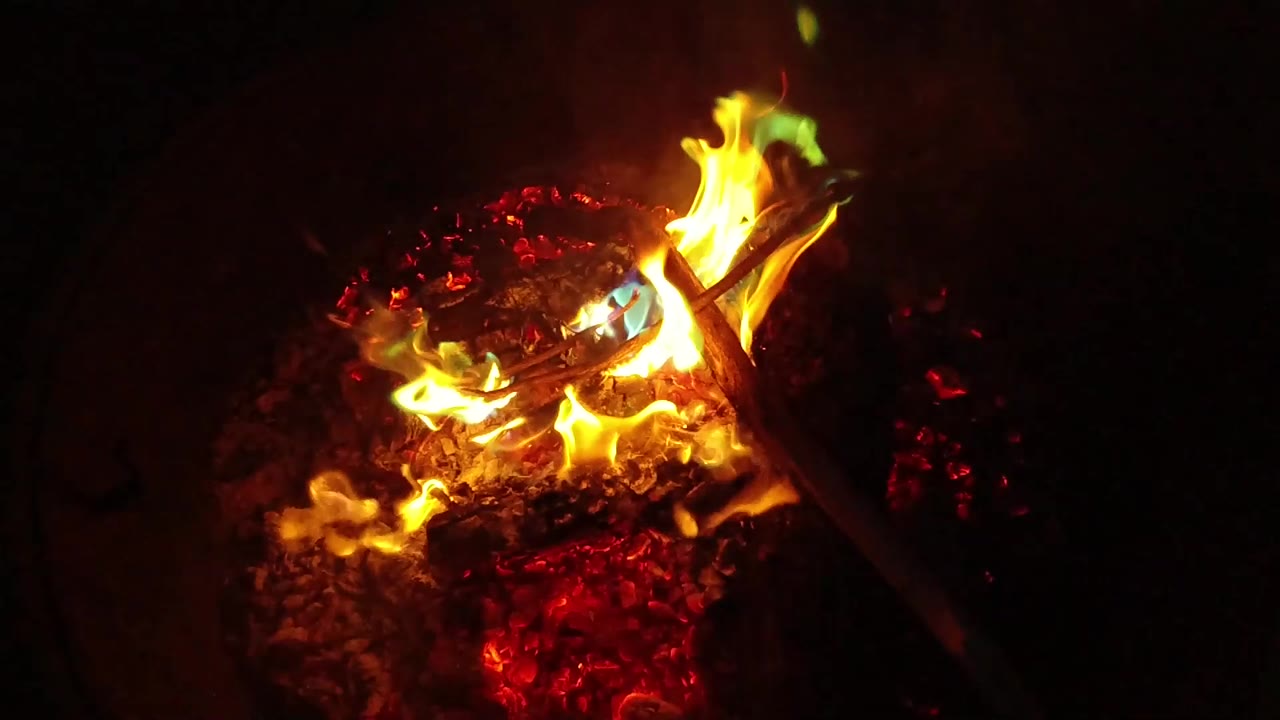 Flames rising from embers beside a diagonal stick.