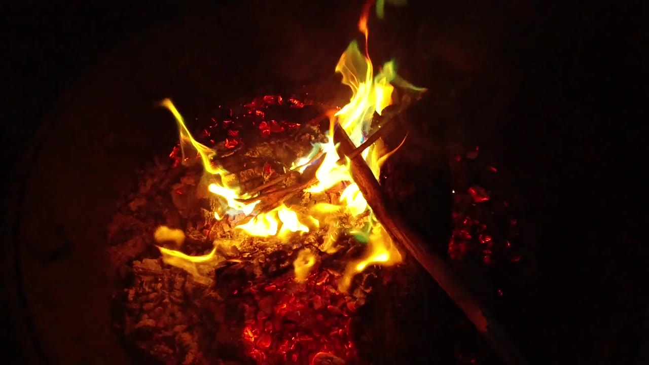 At 0:02, curling yellow flames wrap around the right side of a stick above glowing ash in San Clemente, California, with no visible people.
