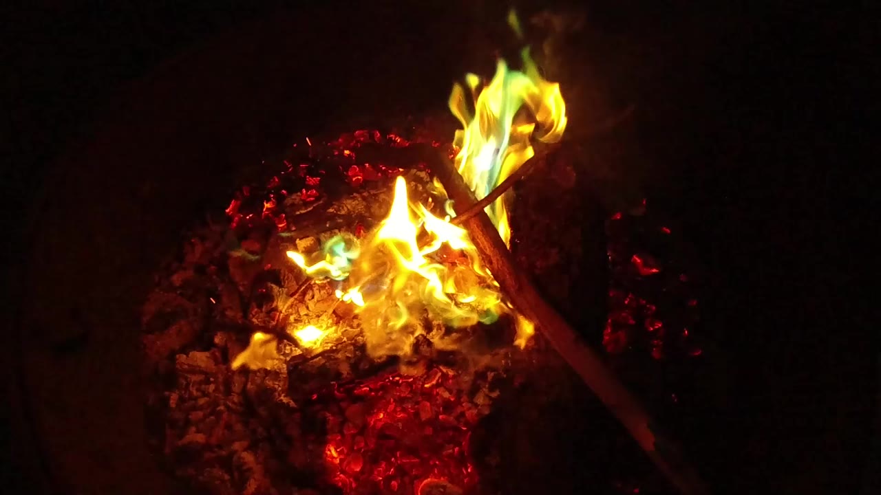 At 0:00, yellow and orange flames burn over red embers in San Clemente, California, with a dark stick crossing the fire and no visible people.