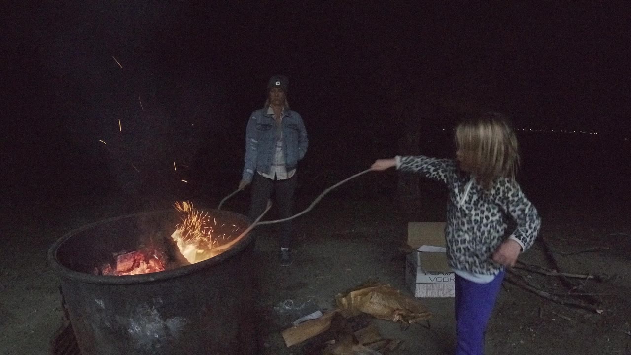 In San Clemente, California, the girl holds the stick over brighter flames and sparks while the adult remains centered behind the fire pit.