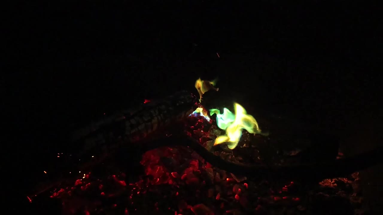 At 0:00, small green-yellow flames lick over red campfire embers and stacked wood in San Clemente, California, with no visible people.