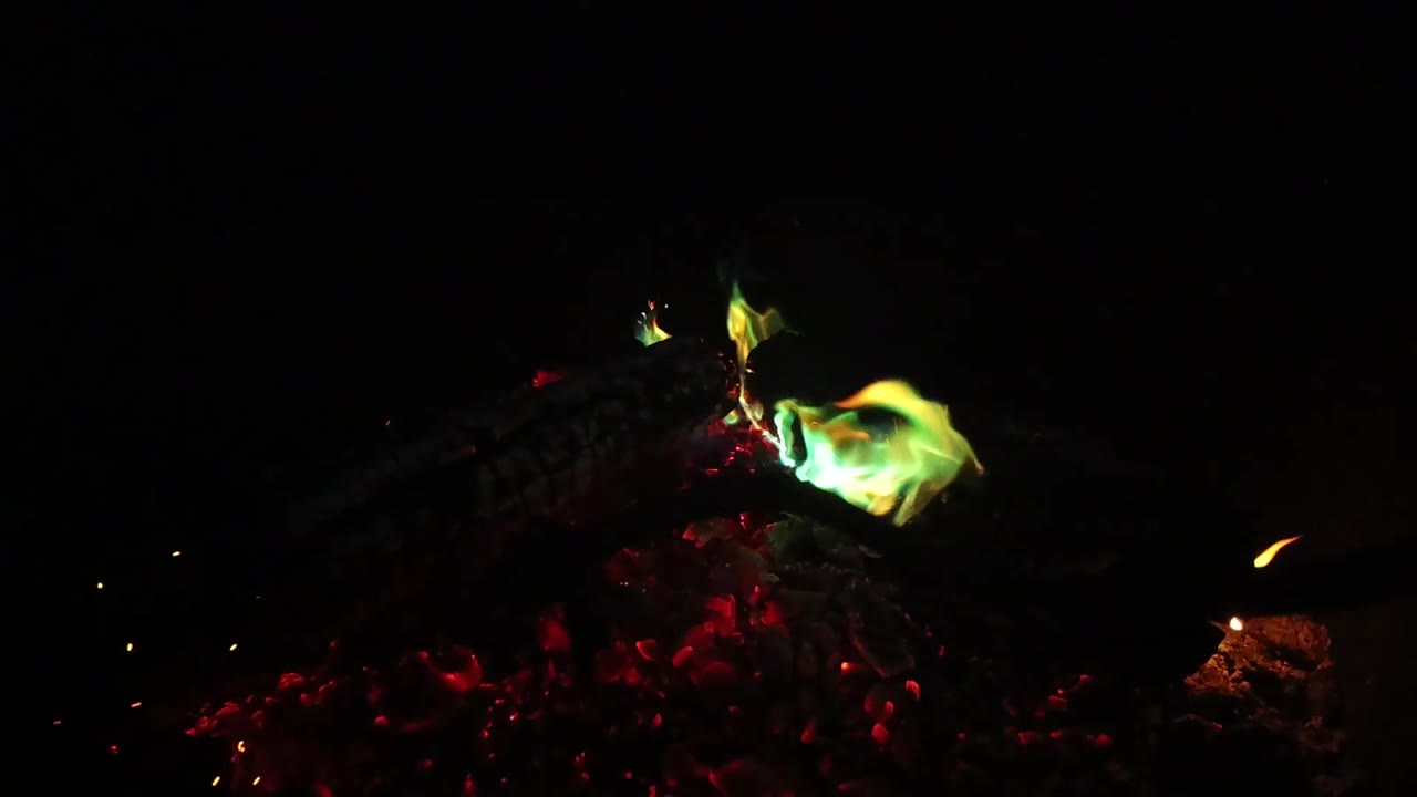 At 0:02, the campfire flame sits lower over the red embers and small sparks appear against the black San Clemente night background, with no visible people.