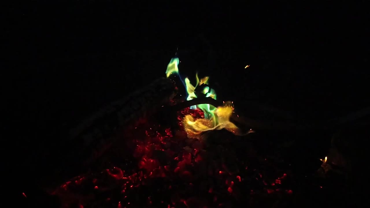 A brighter yellow-orange flame curls to the right over red embers and dark branch shapes in San Clemente, California, with no visible people.