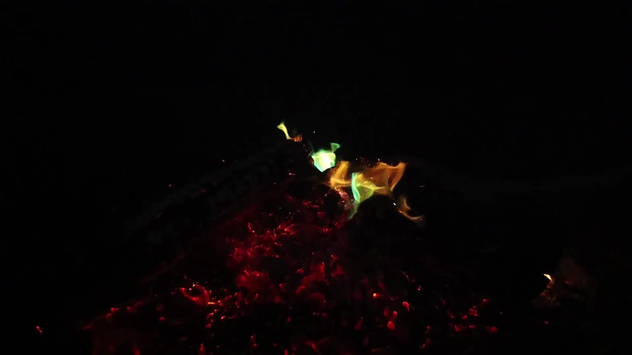 A low yellow-green flame sits near the left side of a red ember cluster in San Clemente, California, surrounded by deep black space and no visible people.