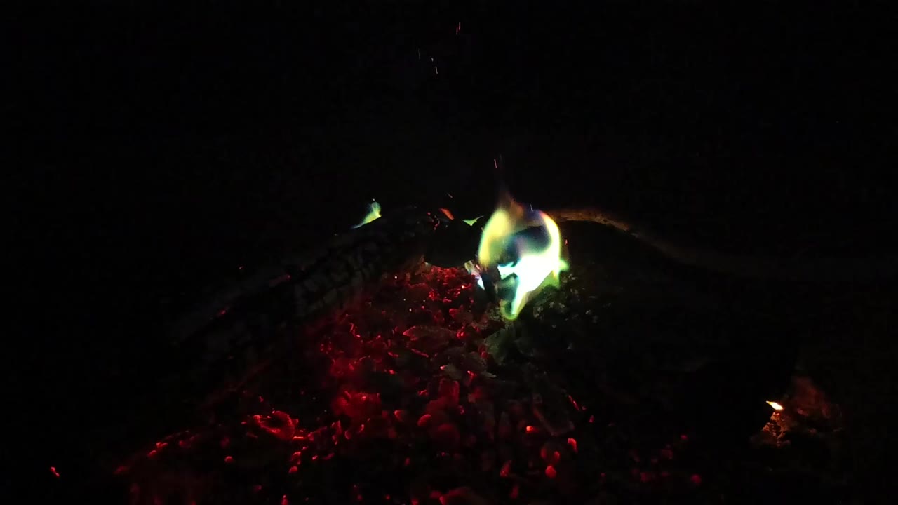 One second into the San Clemente clip, the flame leans over the glowing red coal bed while the surrounding frame remains nearly black, with no visible people.