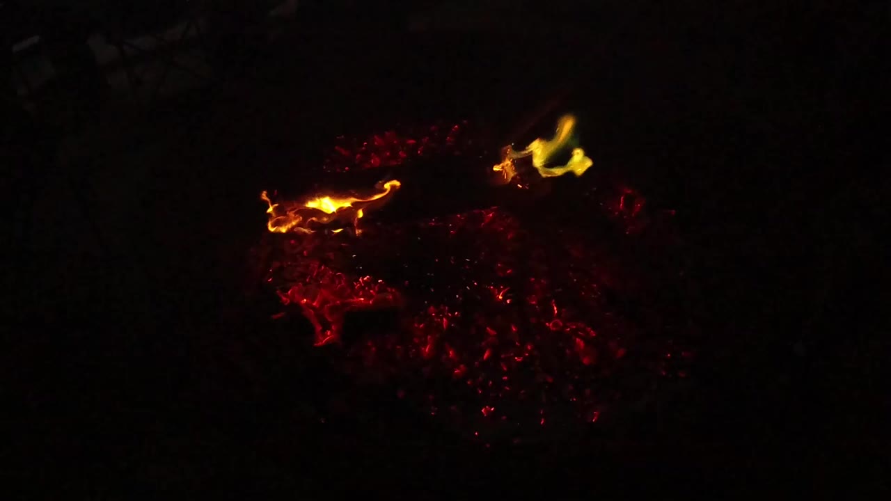 At 0:00, small yellow flames rise above red coals in a dark close-up from San Clemente, California, with no visible people.