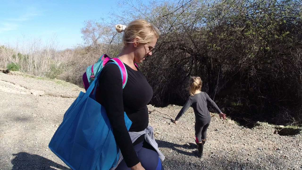 In San Clemente, California, the woman is closer to the right edge of frame while the child walks ahead along the road beside shadowed brush.