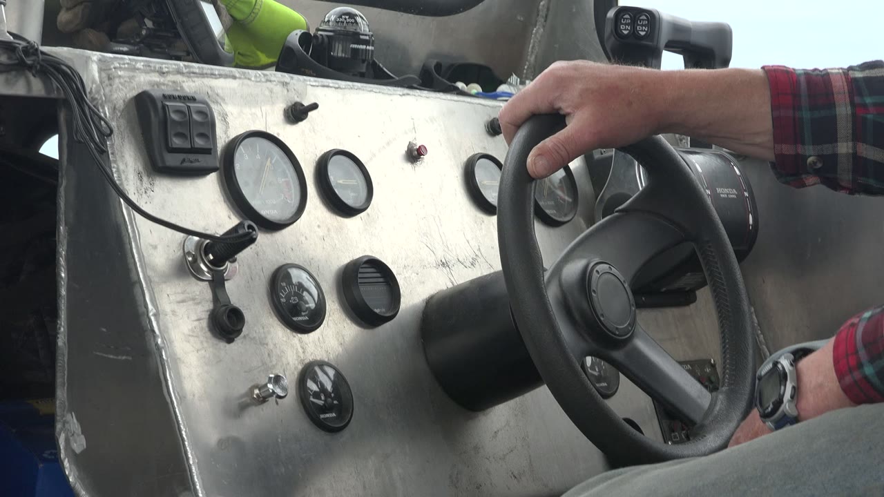 At 0:00 in Red Lake, Canada, a plaid-sleeved hand grips the steering wheel beside a scratched metal dashboard with round gauges and switches, with no faces visible.