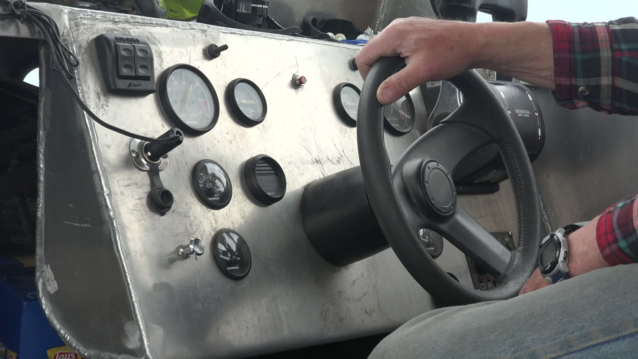At 0:01 in Red Lake, Canada, the steering wheel sits slightly right of center with the driver's hand at the top and analog gauges spread across the metal panel, with no faces visible.