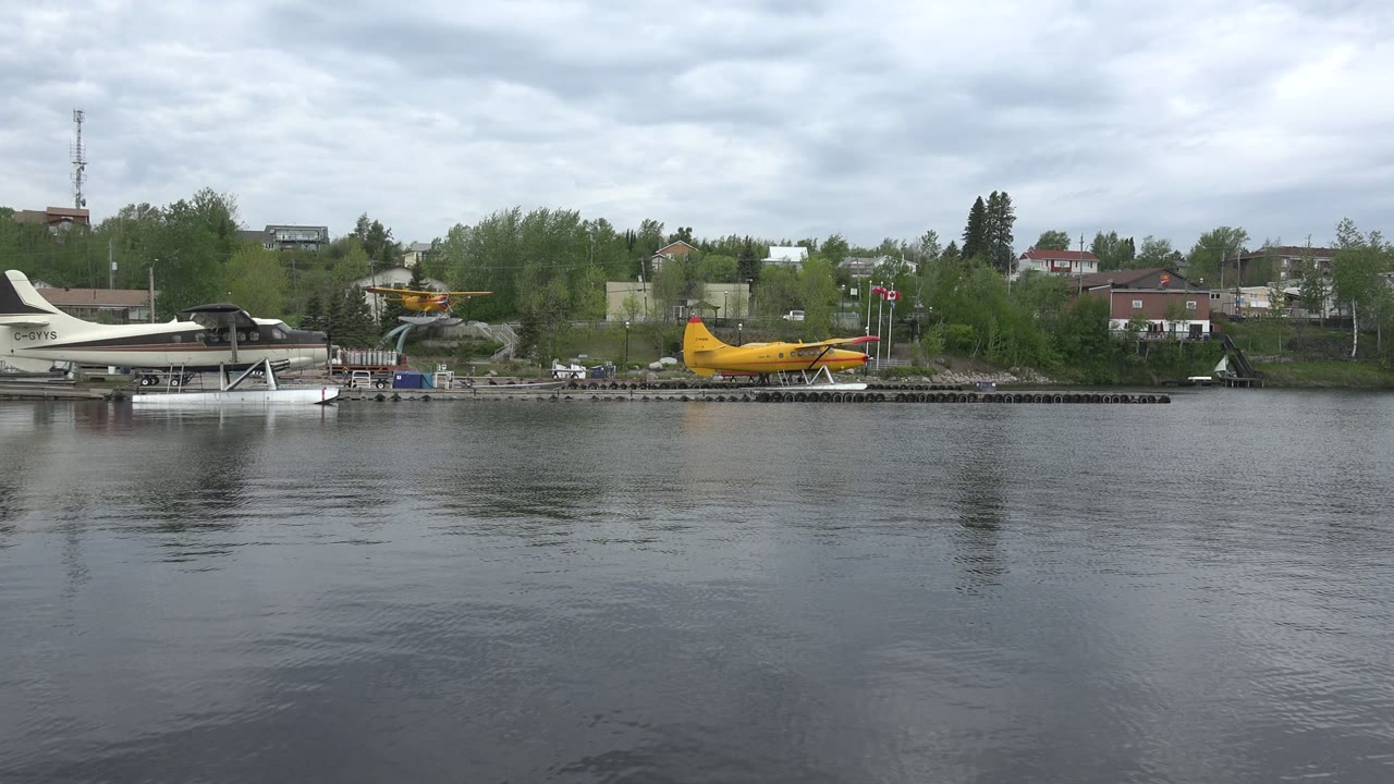 Wide lake view with distant docks, seaplanes, trees, and shore buildings.
