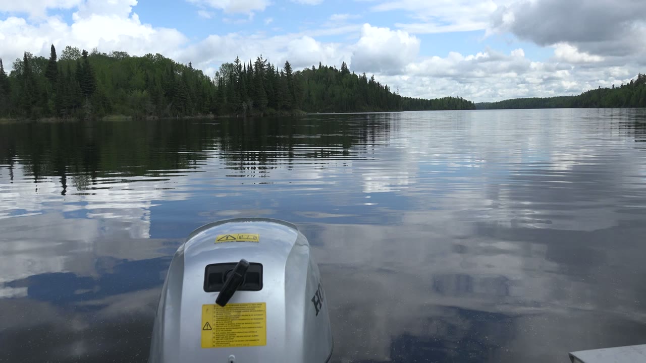 At 0:01, the motor remains centered low in frame as the Red Lake, Canada shoreline opens across the horizon, with ripples interrupting the cloud reflections and no visible people.