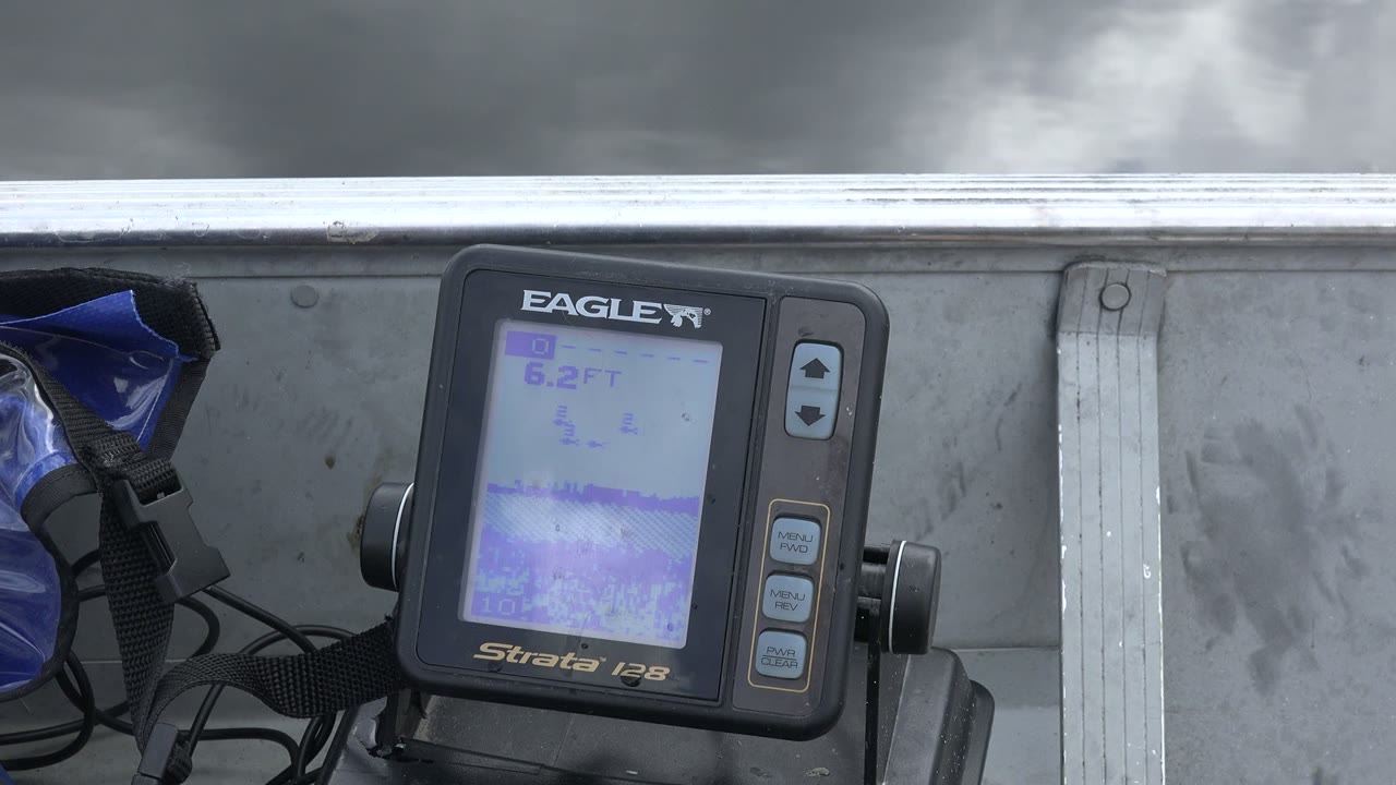 At 0:01 in Red Lake, Canada, the monitor remains centered beside blue gear, black straps, and a pale metal boat rail, with gray sky filling the upper frame and no visible people.
