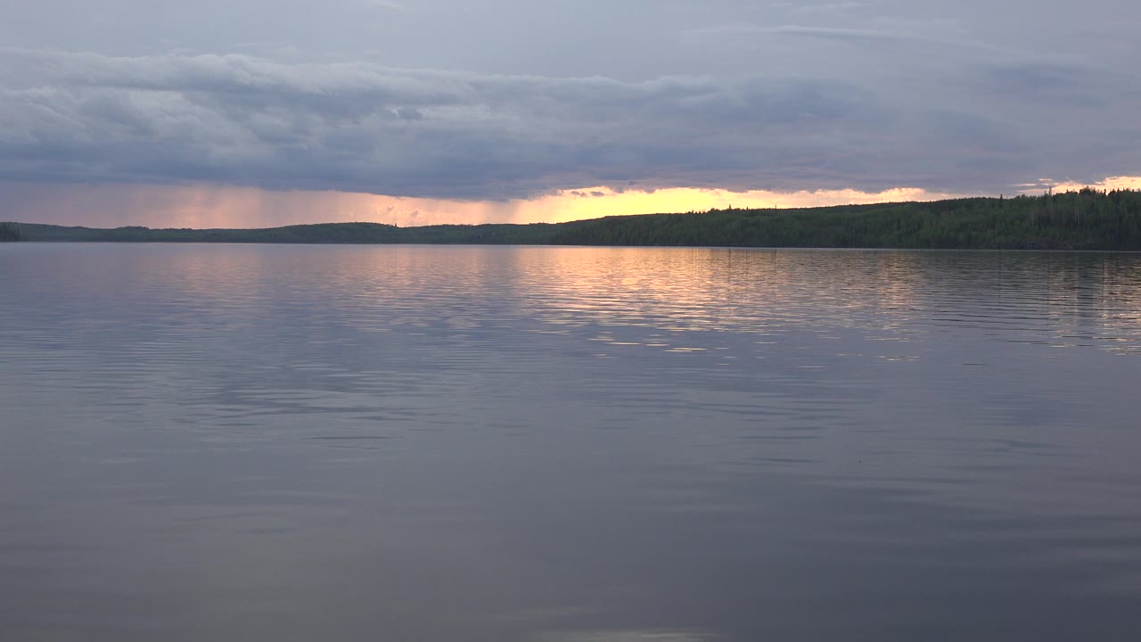 Red Lake, Canada at 0:01 shows a wider orange reflection on the lake surface, the distant shore staying dark, heavy cloud cover overhead, and no visible people.