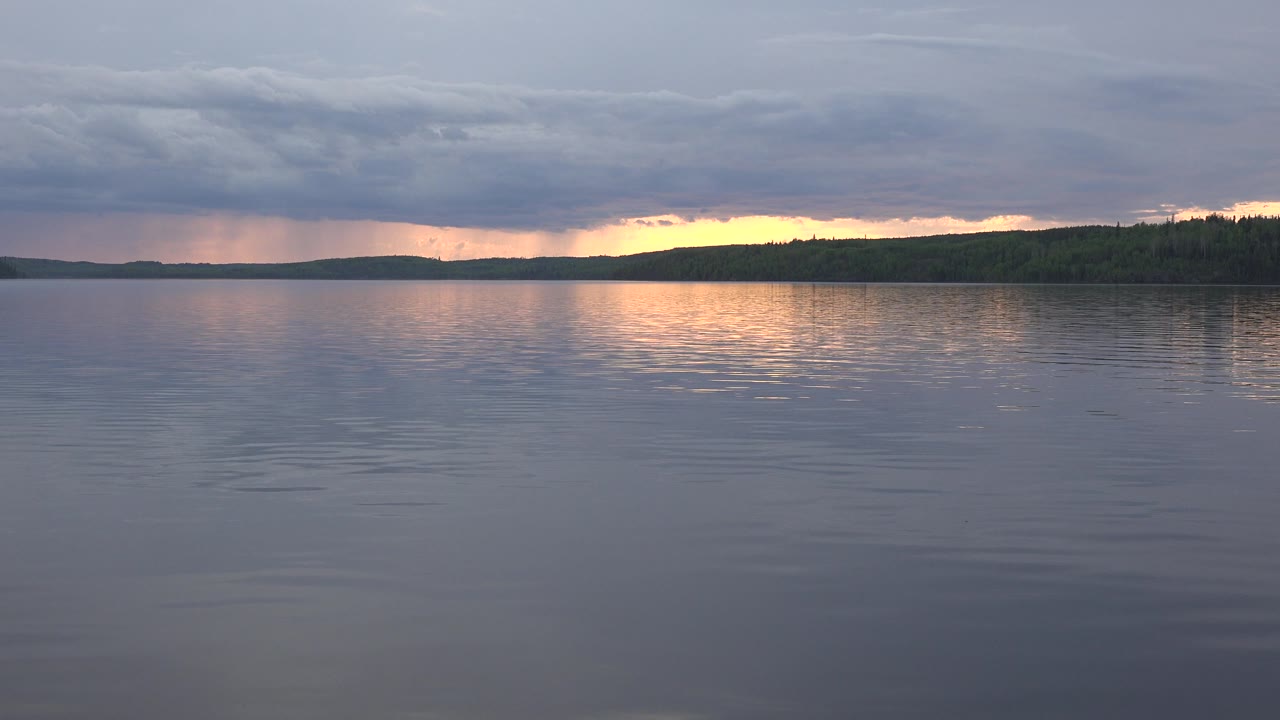 Distant forest shoreline below storm clouds at sunset over a lake