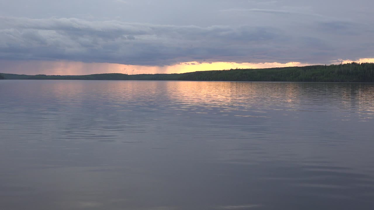 Opening frame of Red Lake, Canada with blue-gray rippled water, a low dark shoreline, warm sunset light under heavy clouds, and no visible people.